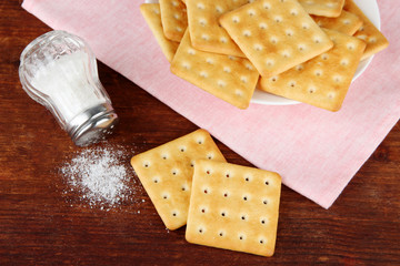 Delicious crackers with salt and napkin on wooden background