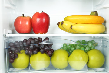Milk bottles, vegetables and fruits in open refrigerator.