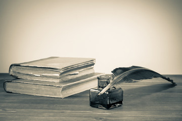 Quill pen, ink bottle, old books on table for vintage background