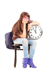 Sad female student sitting on a chair and holding a clock