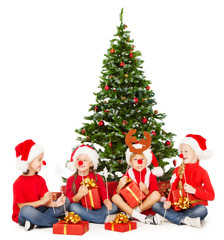 Christmas children in Santa hat playing presents under fir tree