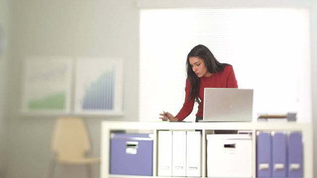 Hispanic business woman working at laptop with co workers in bac