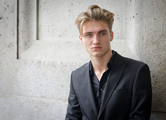 Attractive blond young man in jacket, against a wall - obrazy, fototapety, plakaty