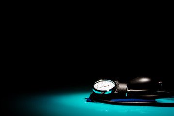 Sphygmomanometer on blue, reflective table and black background