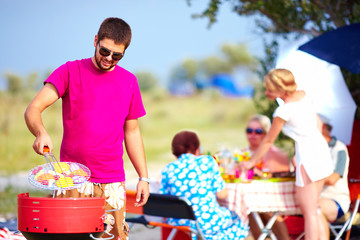 happy man cooks vegetables on the grill, family picnic