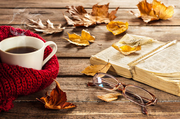 Hot coffee, book, glasses and autumn leaves on wood