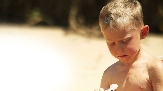 Little boy eats yogurt on the sunny beach