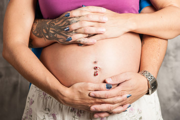 Fototapeta na wymiar Tattoed man and woman interlock fingers over baby belly