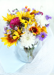 Bouquet of wild flowers in glass vase on light background