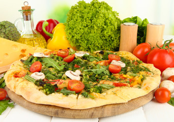 Tasty vegetarian pizza and vegetables on wooden table