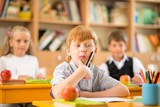 Little redhead schoolboy behind school desk 
