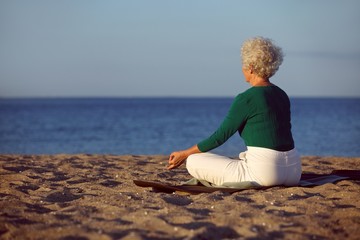 Elder woman doing yoga meditation on beach