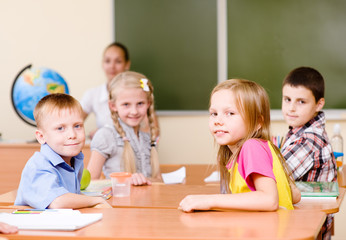 Fototapeta premium Portrait of schoolkids at workplace with teacher on background