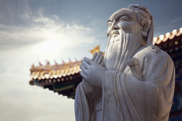 Close-up of stone statue of Confucius, pagoda roof in the background