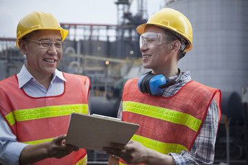 Two engineers in protective workwear standing and laughing outside of a factory