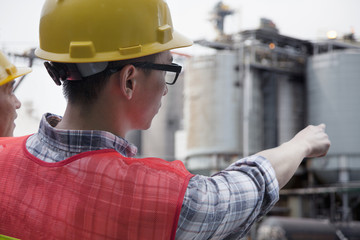 Two engineers in protective workwear pointing outside of a factory