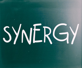 The word "Synergy" handwritten with white chalk on a blackboard
