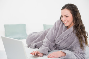 Relaxed brunette in bathrobe using laptop in bed