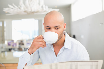 Man drinking coffee while reading newspaper at home