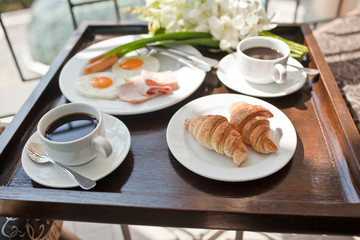 breakfast with cup of black coffee, eggs and croissants on balco