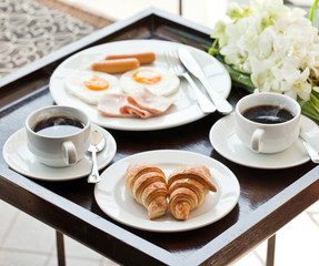 breakfast with cup of black coffee, eggs and croissants on balco