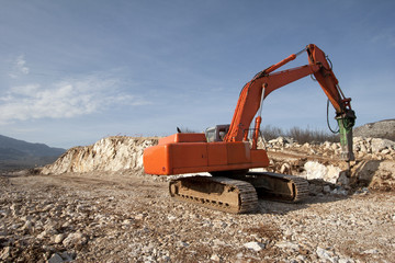 Orange backhoe drilling stone soil on construction of road