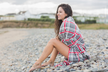 Smiling woman covered with blanket at the beach