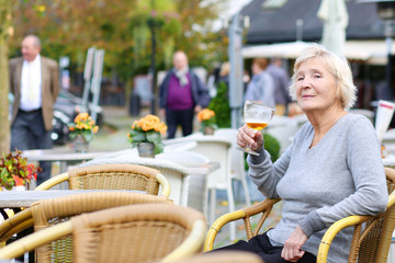 Happy senior woman drinking beer outdoors in the cafe