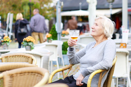 Happy Senior Woman Drinking Beer Outdoors In The Cafe