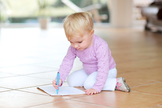 Cute toddler draws with colorful pencils sitting on tiles floor