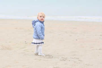 Funny little baby girl walks on peaceful sandy beach 