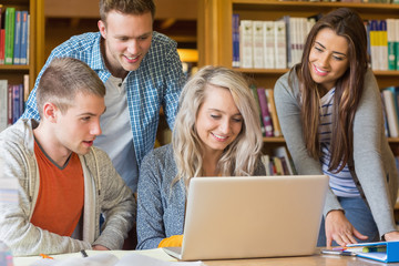 Happy students using laptop at desk in library