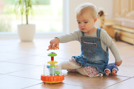 Cute little baby girl plays with toys sitting indoors