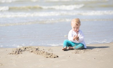 One year old baby girl plays on the beach