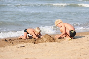 Two active brothers playing with sand on the beach