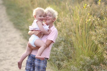 Loving teeneger boy holding his baby sister in the dunes