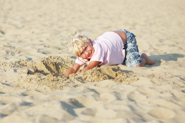 Happy teenager boy digging big hole in sand on a beach
