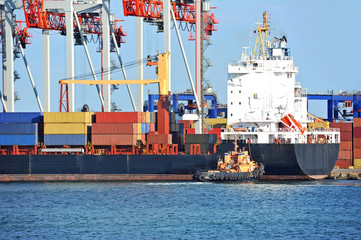 Tugboat assisting container cargo ship to harbor quayside