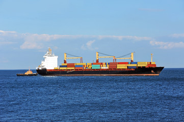 Tugboat assisting container cargo ship to harbor quayside