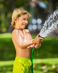 Child, boy or kid plays with water hose outdoors