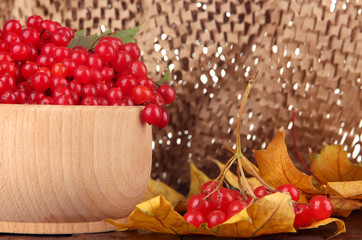 Red berries of viburnum in wooden bowl with yellow leaves
