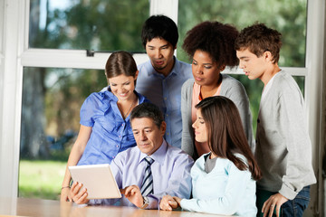 Teacher Using Digital Tablet While Students Standing Around Him