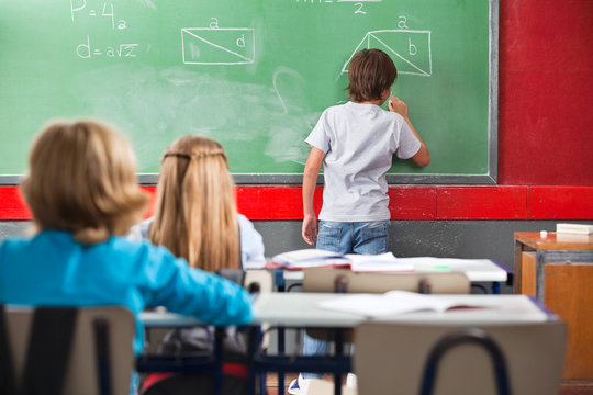 Schoolboy Writing On Greenboard In Classroom