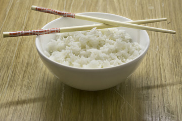 Bowl of white rice with chopsticks, wooden background