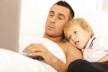 Father and son surfing on their computers on the bed at home