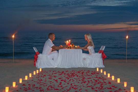 Young couple share a romantic dinner with candles, torches and w