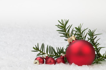 rote Christbaumkugeln mit Tannenzweig im Schnee