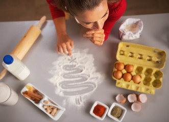 Thoughtful housewife drawing christmas tree on kitchen table