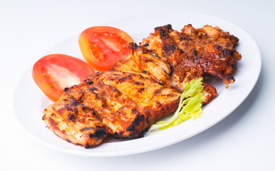 Grilled chicken on a white plate with vegetables on background.