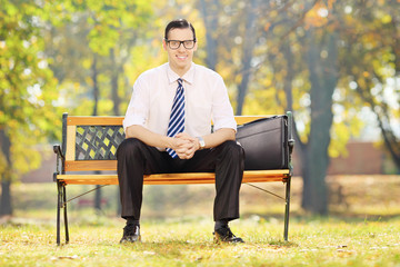 Smiling young businessman sitting on bench on a sunny day